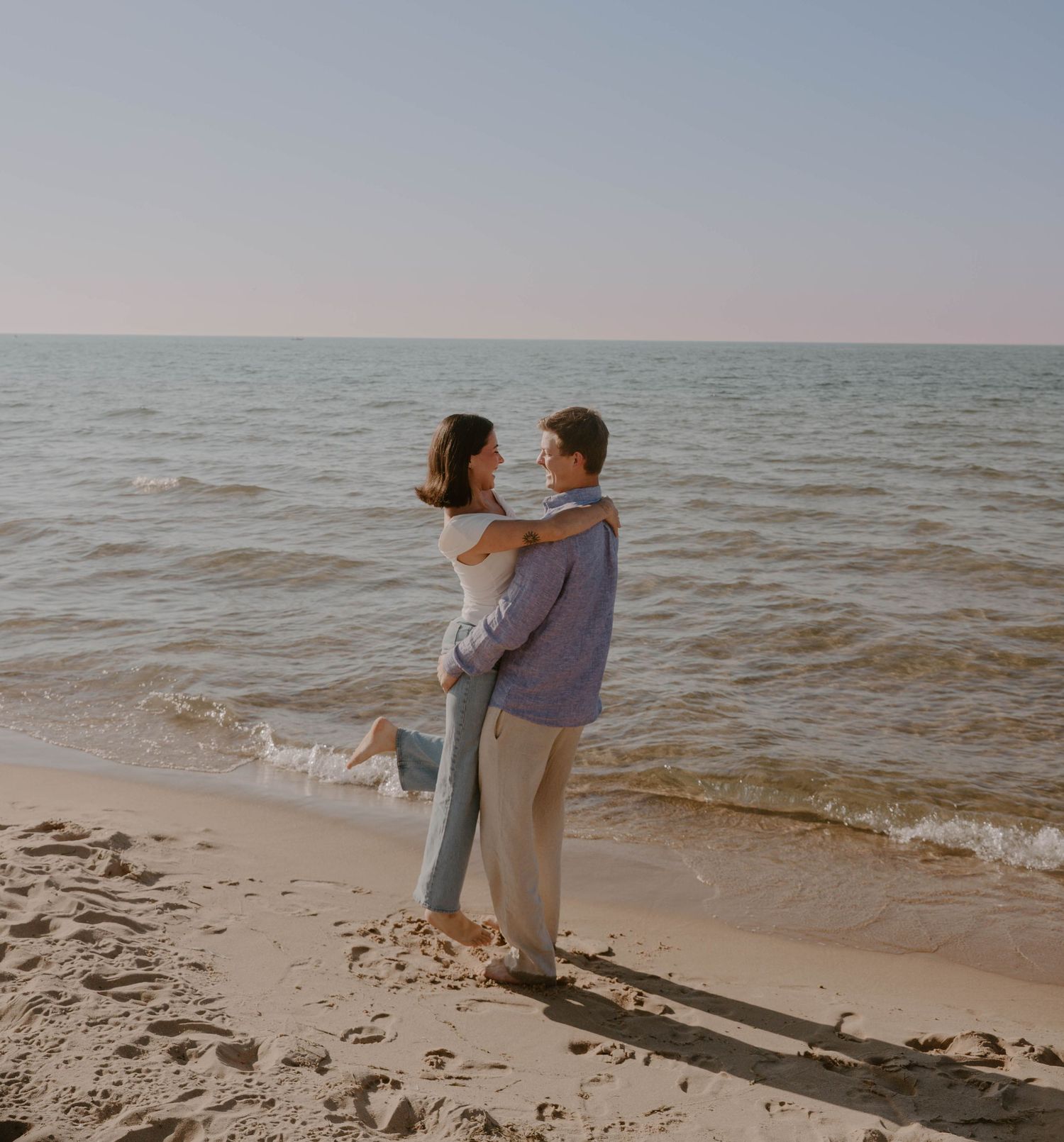 A couple shares a romantic moment on a sandy beach with gentle waves in the background.
