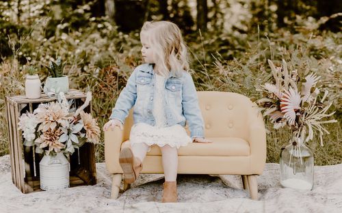 A cozy outdoor seating vignette with a beige loveseat, floral arrangements, and natural surroundings.