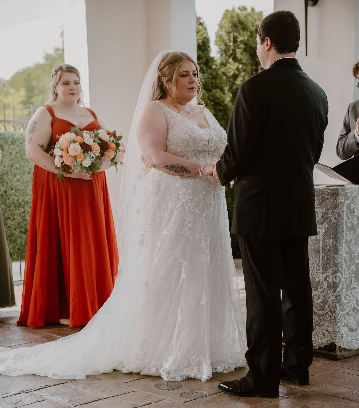 Wedding party stands in formation with bridesmaids in red dresses and groomsmen in formal attire during outdoor ceremony.