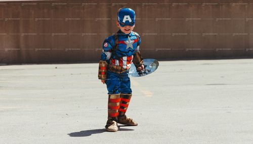 A child dressed as Captain America poses against a concrete wall.