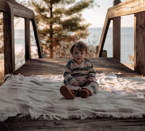 Toddler sitting on a white blanket on wooden deck overlooking scenic landscape at sunset.