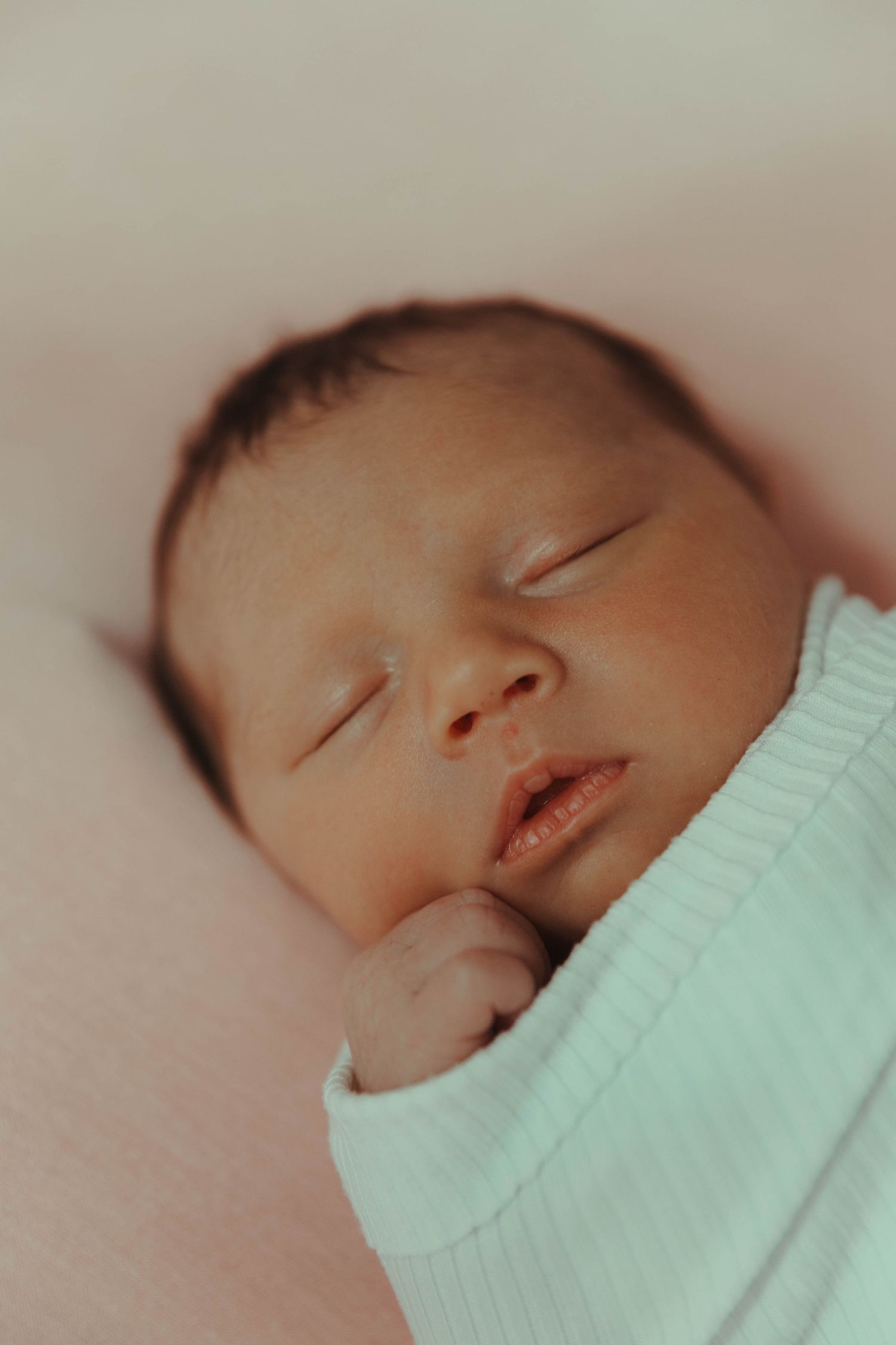 A sleeping baby in a mint green sweater rests peacefully against a soft pink background.