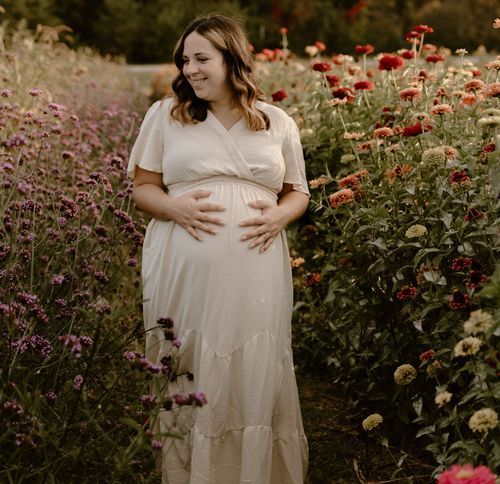 A person in a white dress stands among blooming flowers in a garden during golden hour.