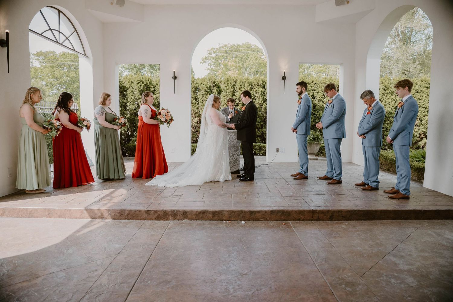 Wedding party stands in an elegant white columned veranda during outdoor ceremony.