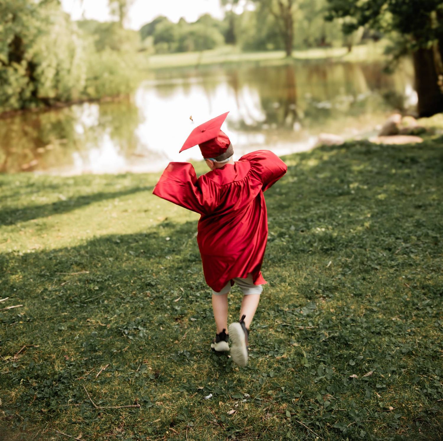 A person in a red dress twirls playfully on a grassy hill near a lake on a sunny afternoon.
