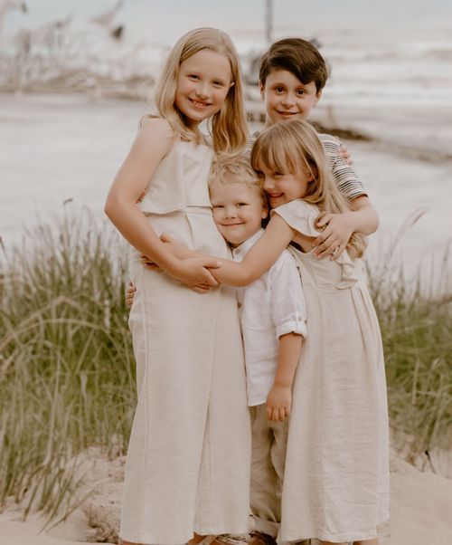 Group portrait of siblings in light colored dresses on beach with coastal vegetation.
