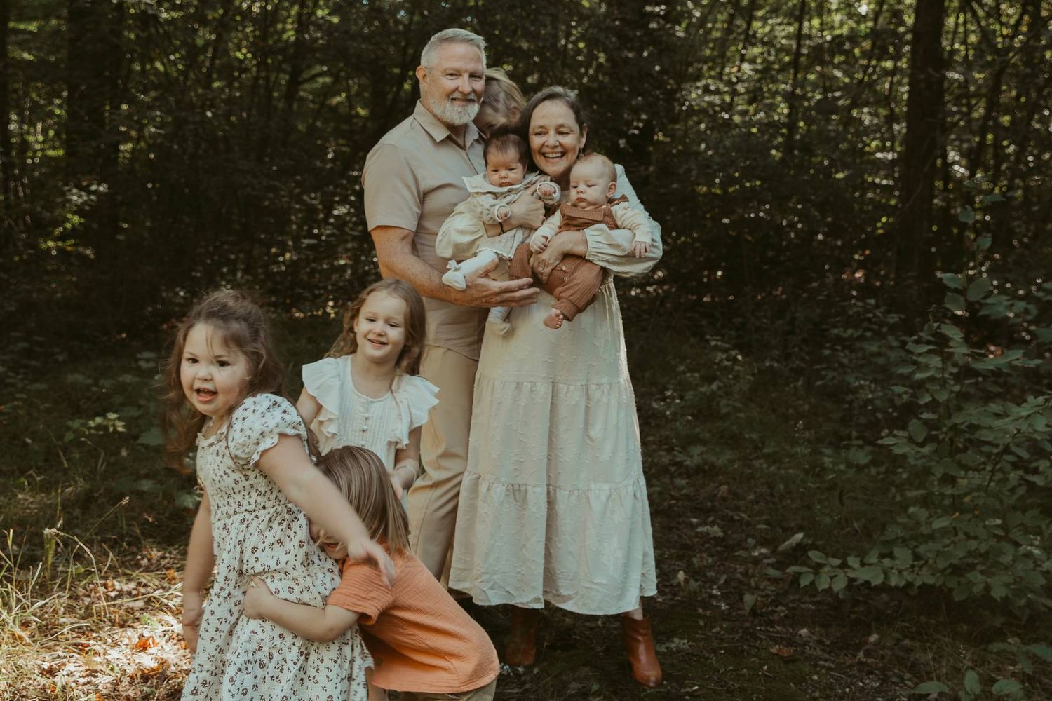 Family of six poses in a lush forest, parents holding babies while young girls embrace in front.