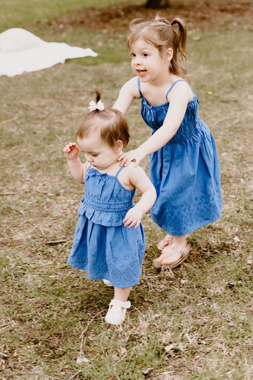 Two children in matching blue dresses playing together outdoors.