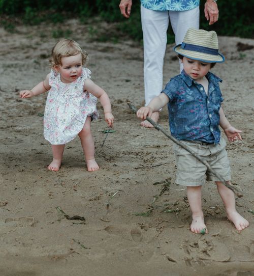 Two children in summer outfits playing barefoot on sandy ground.