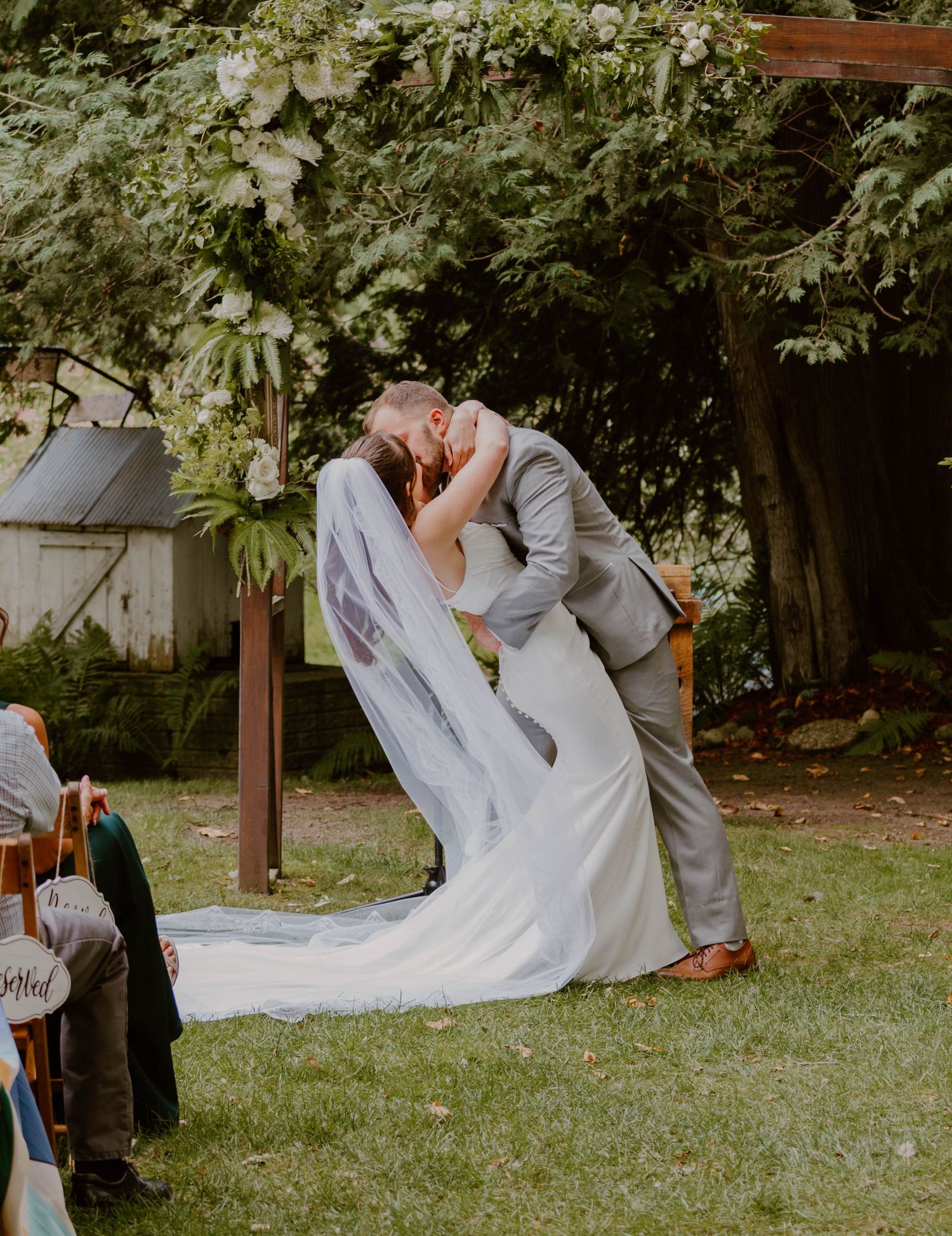 A romantic wedding couple dances and twirls in a garden setting with flowing white dress and grey suit.