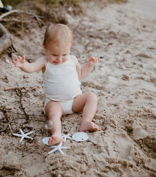 Baby playing with starfish decorations on sandy beach.