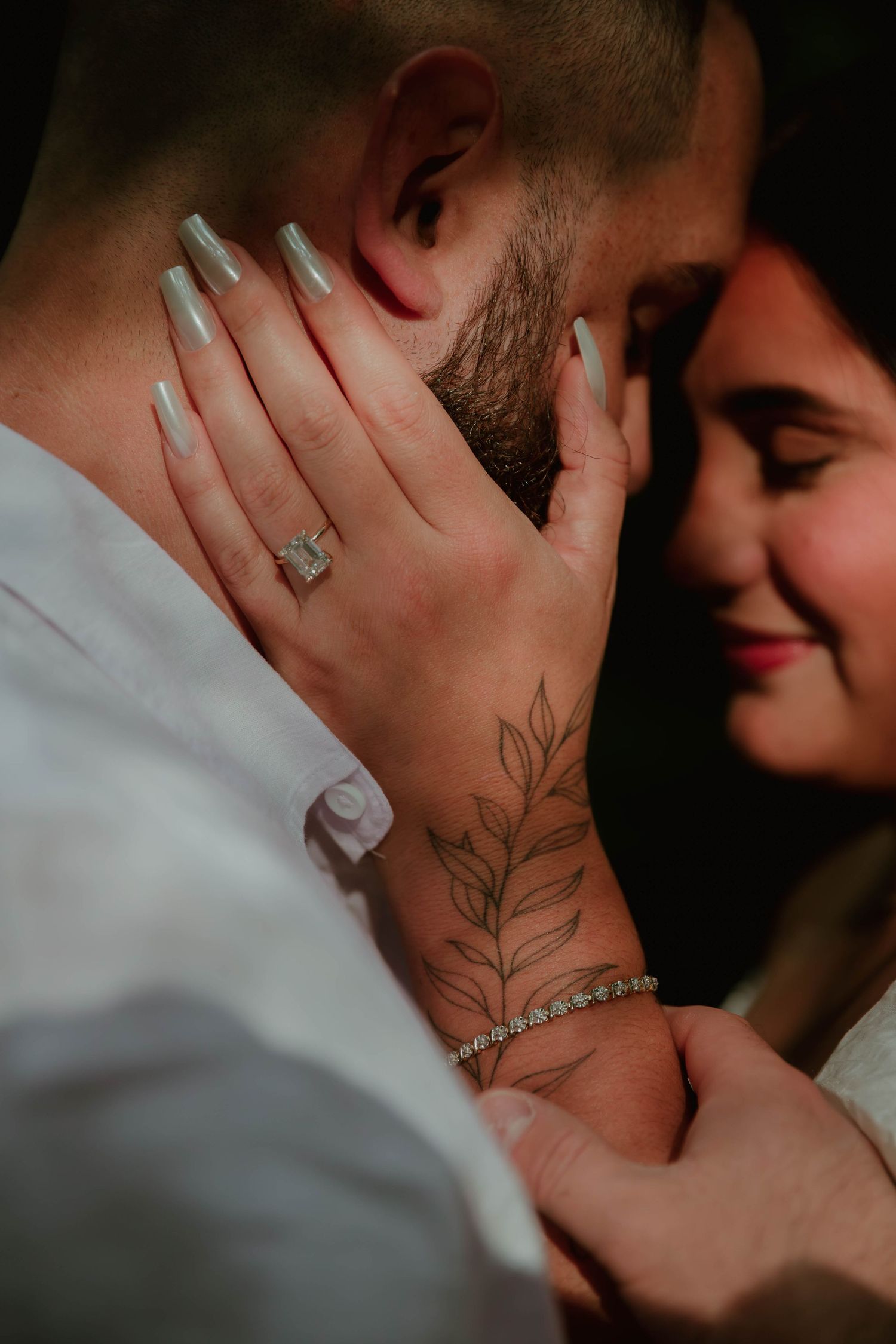 Close-up of couple embracing with engagement ring visible and delicate floral tattoo on wrist.