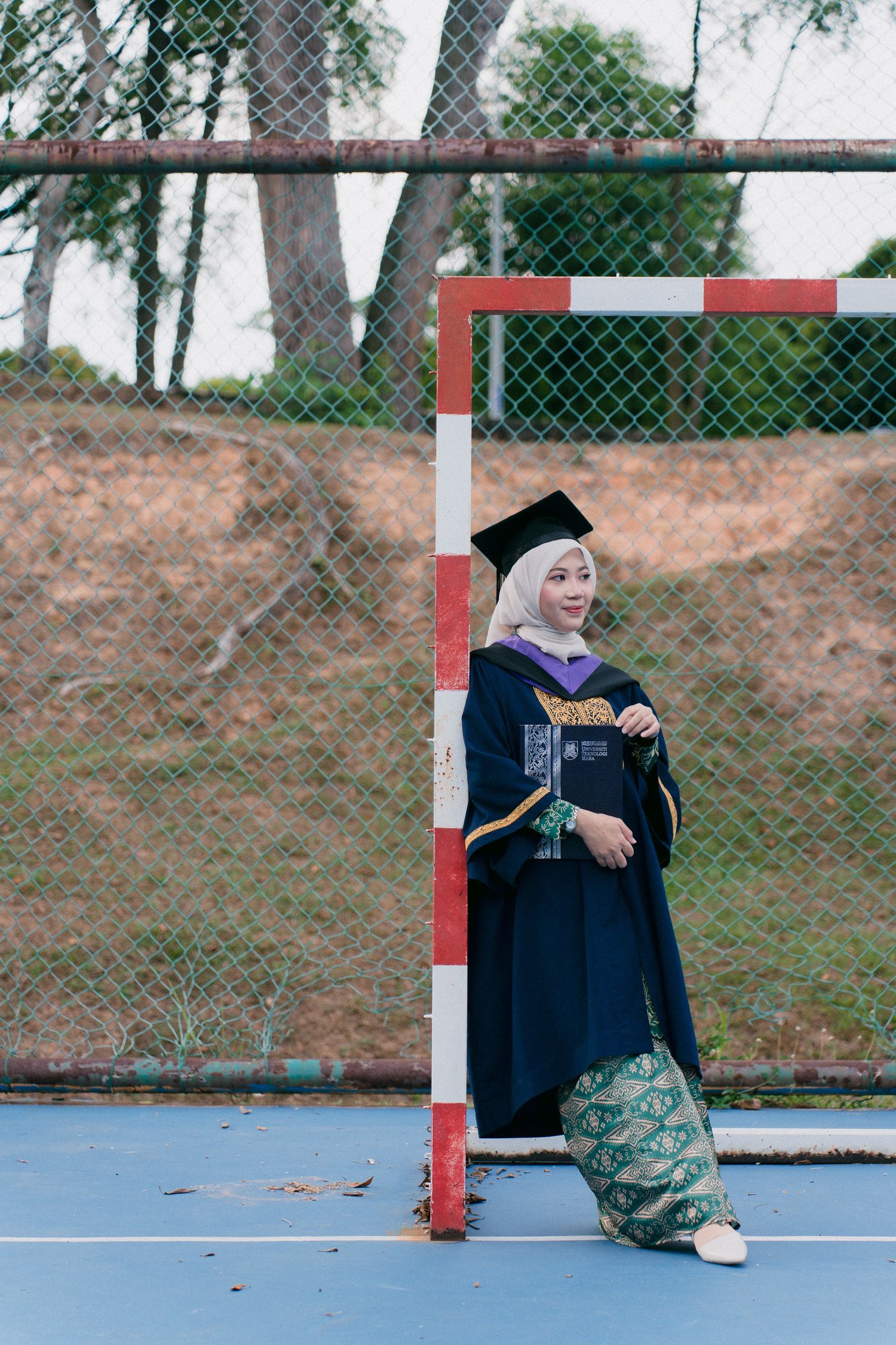 A sequence of photos shows someone in graduation attire posing playfully on a blue sports court outdoors.