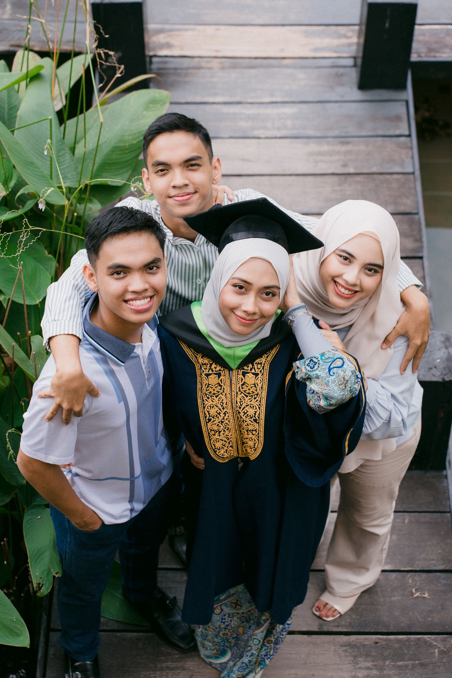 Group of friends in traditional Muslim attire smiling and posing together on wooden deck.