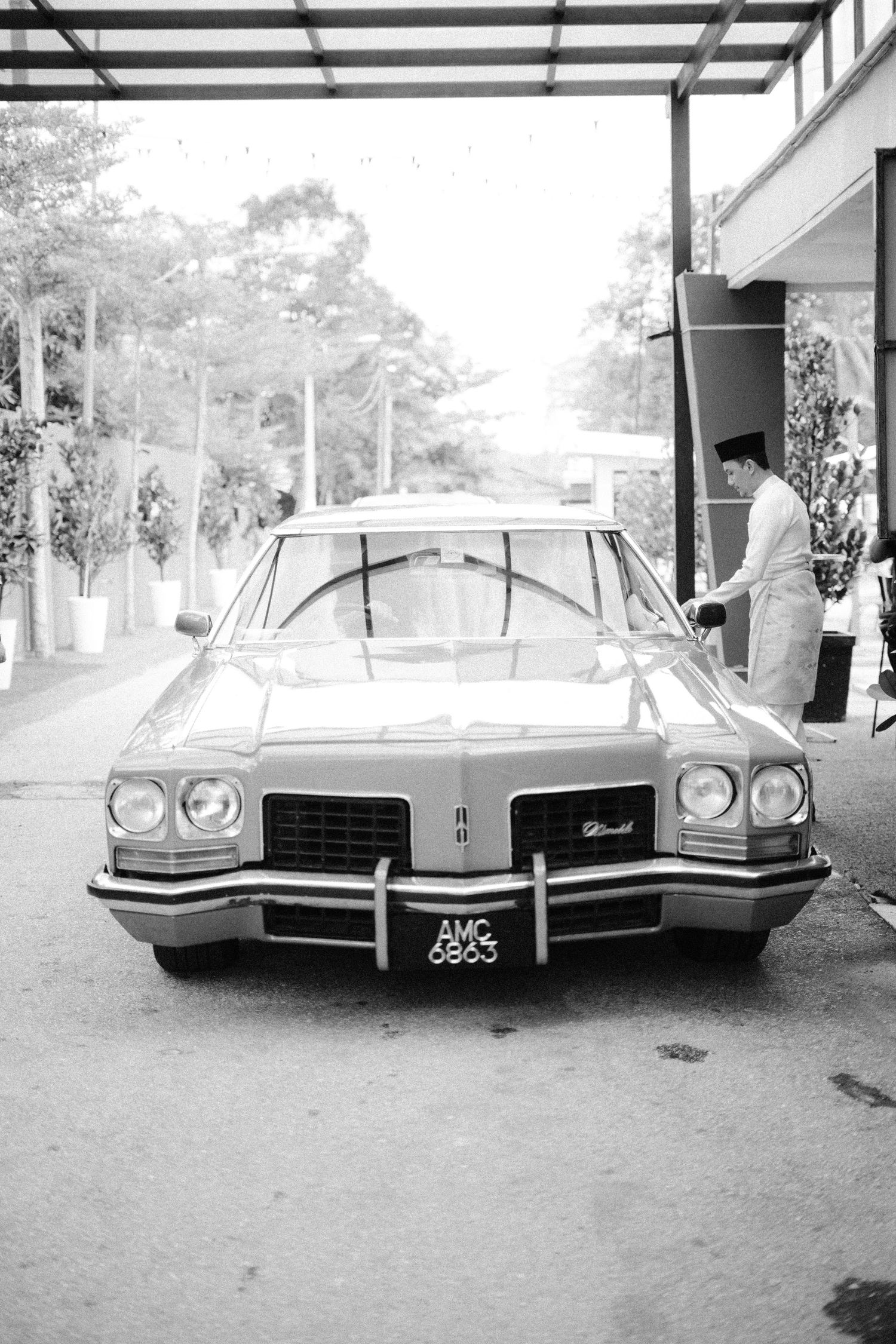 A vintage Pontiac Bonneville sedan parked under a carport in black and white photography.