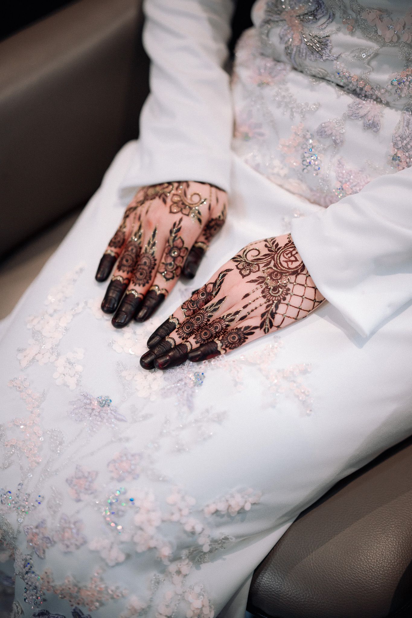 Close-up of a bride's hands adorned with intricate henna mehndi designs, resting on a white embroidered wedding dress.