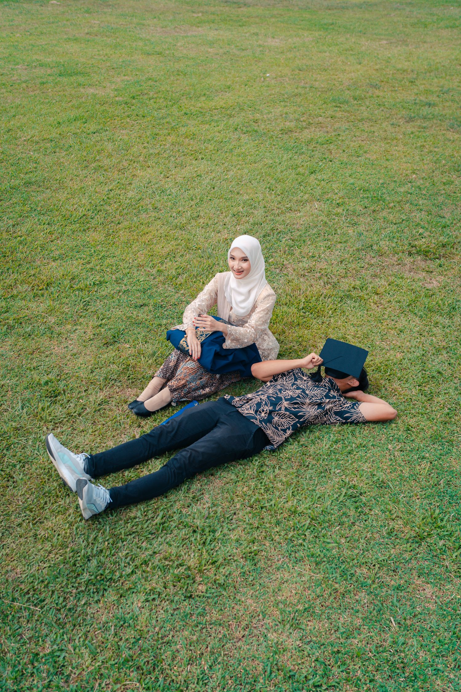 Two friends relaxing on grass lawn during graduation photo shoot.