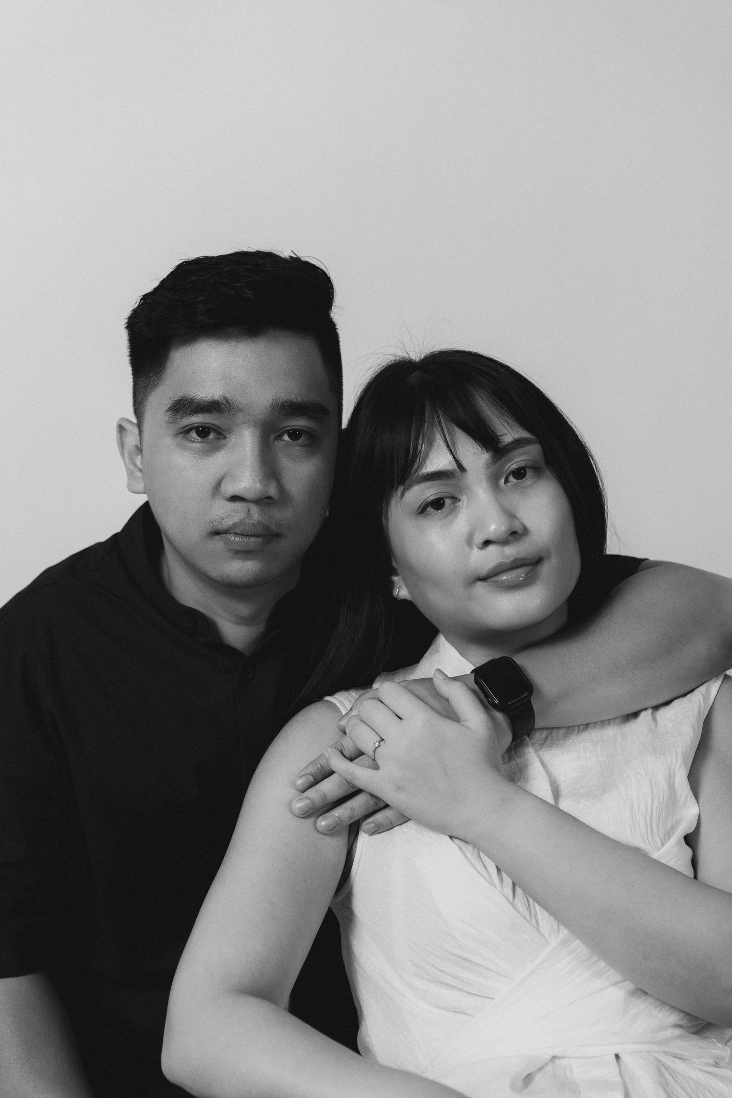 A stylish black and white portrait of a couple posing together in a minimalist studio setting.