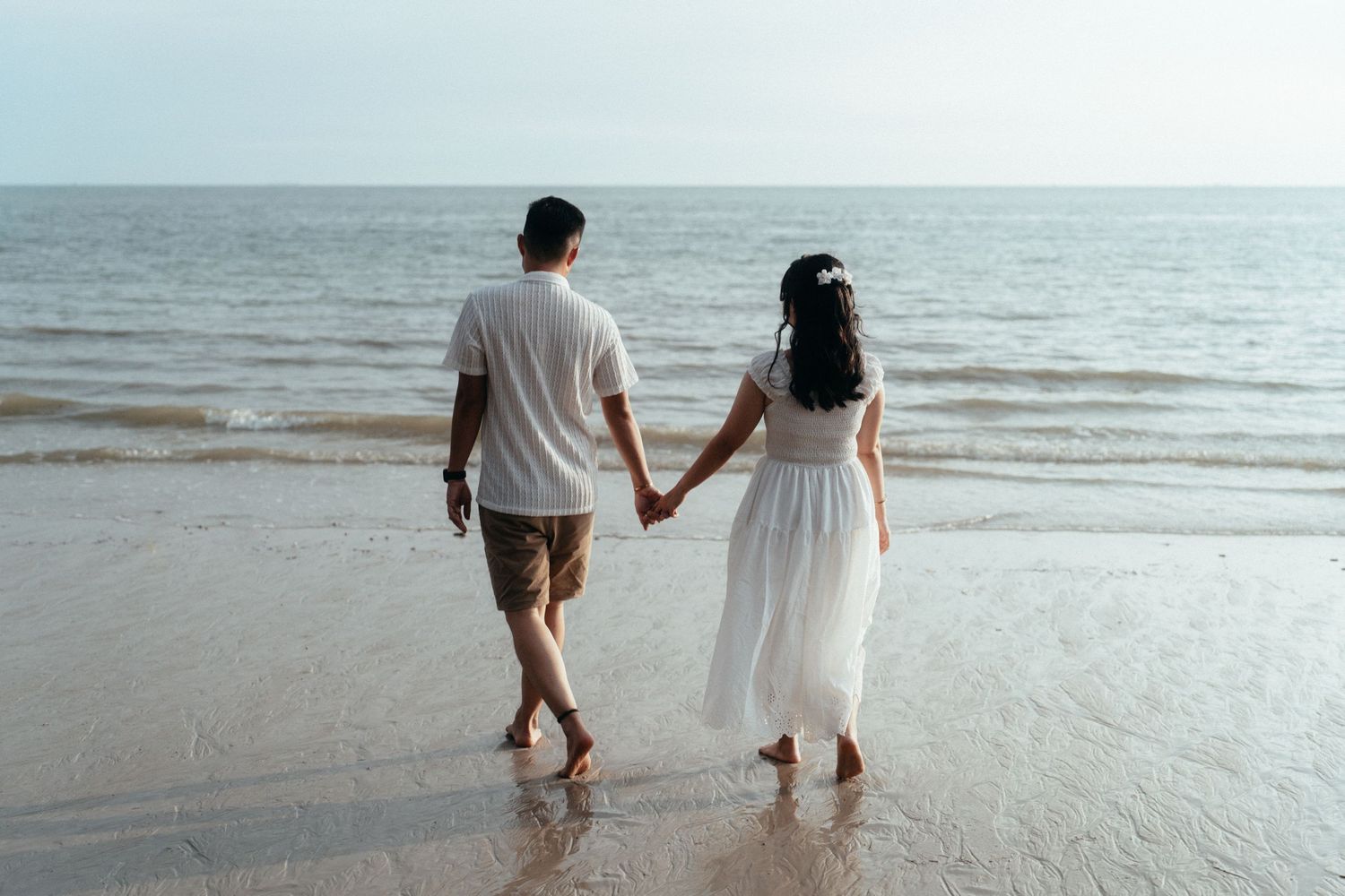 A couple holding hands while walking along the shoreline at the beach.