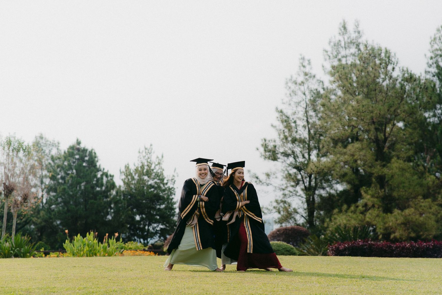 Graduates in black robes strike dynamic poses on a grassy field.