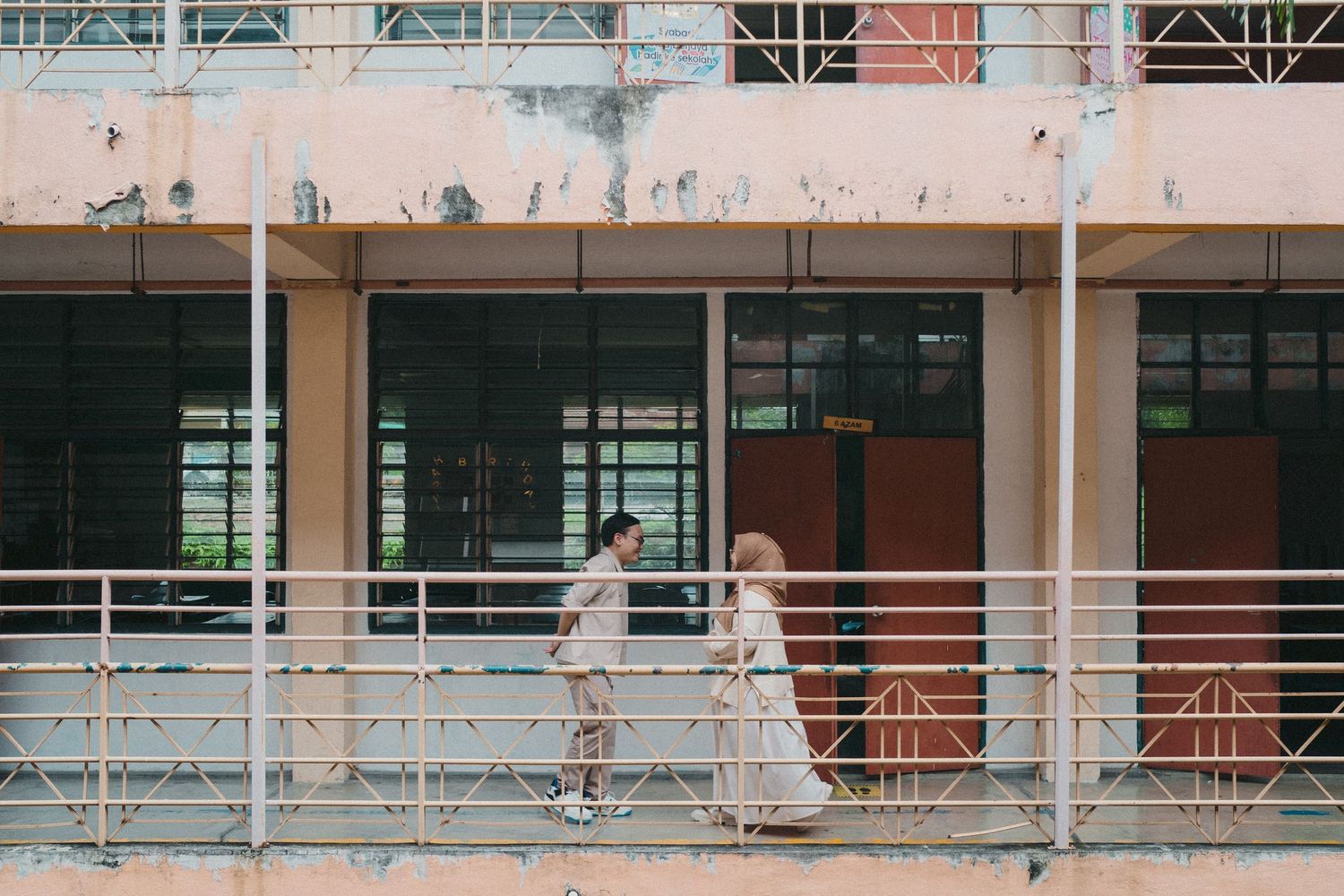 Two students walking along outdoor corridor of educational building with orange tinted walls.