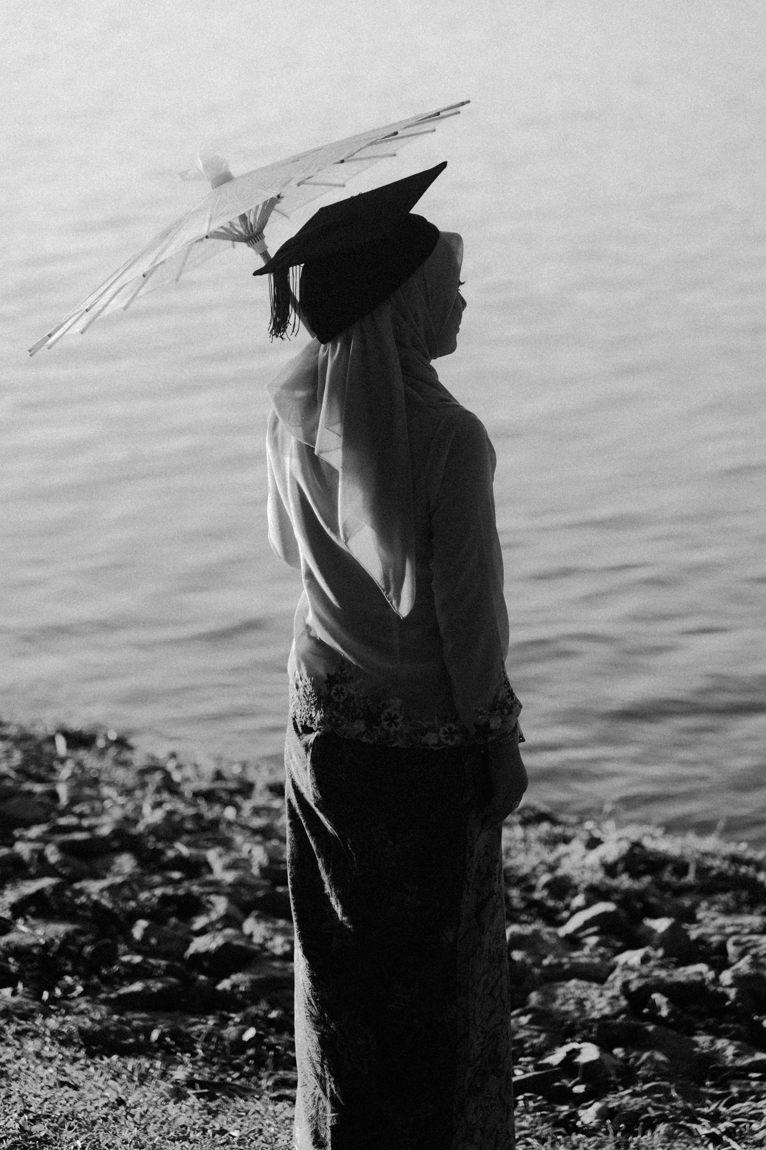 A figure stands at the water's edge in silhouette against rippling waves in a black and white photograph.
