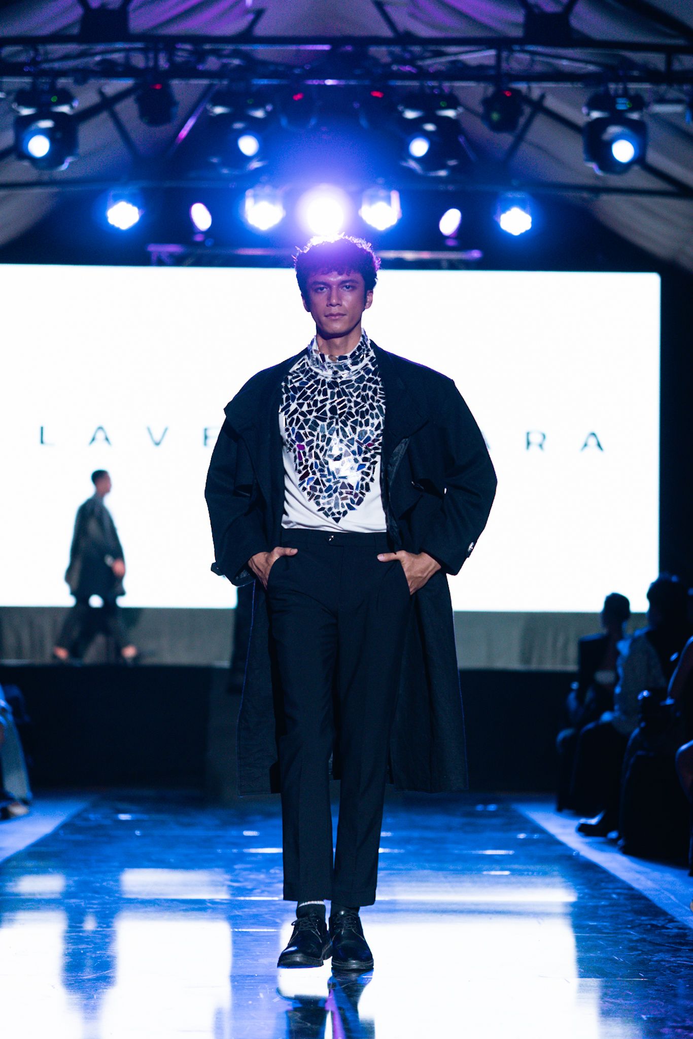 Model in black and white outfit with leopard print detail poses on illuminated runway.
