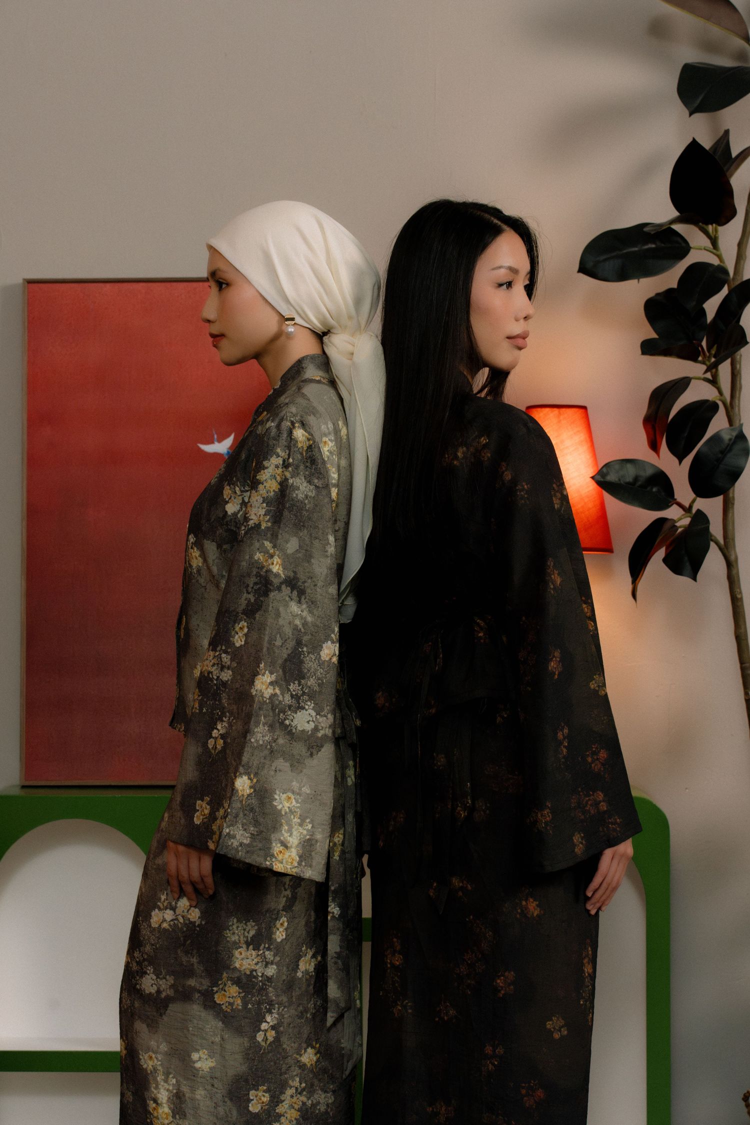 Two figures stand side by side wearing contrasting outfits - one in a floral patterned garment and one in solid black.