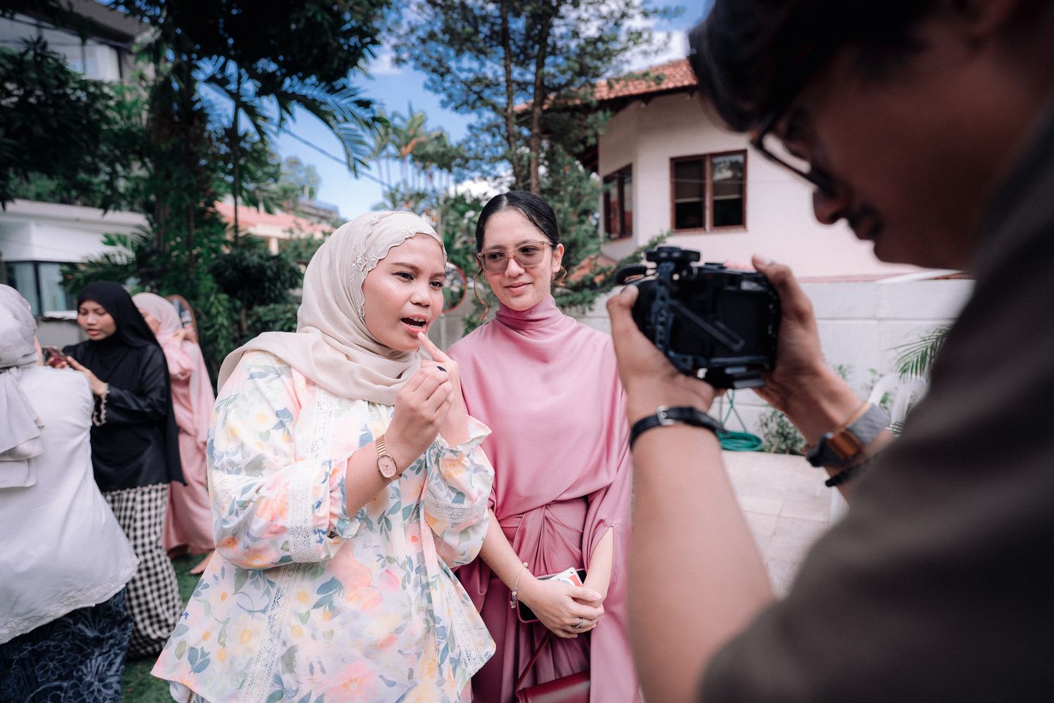 Two women in hijab and modest wear pose for a camera outdoors near a building.