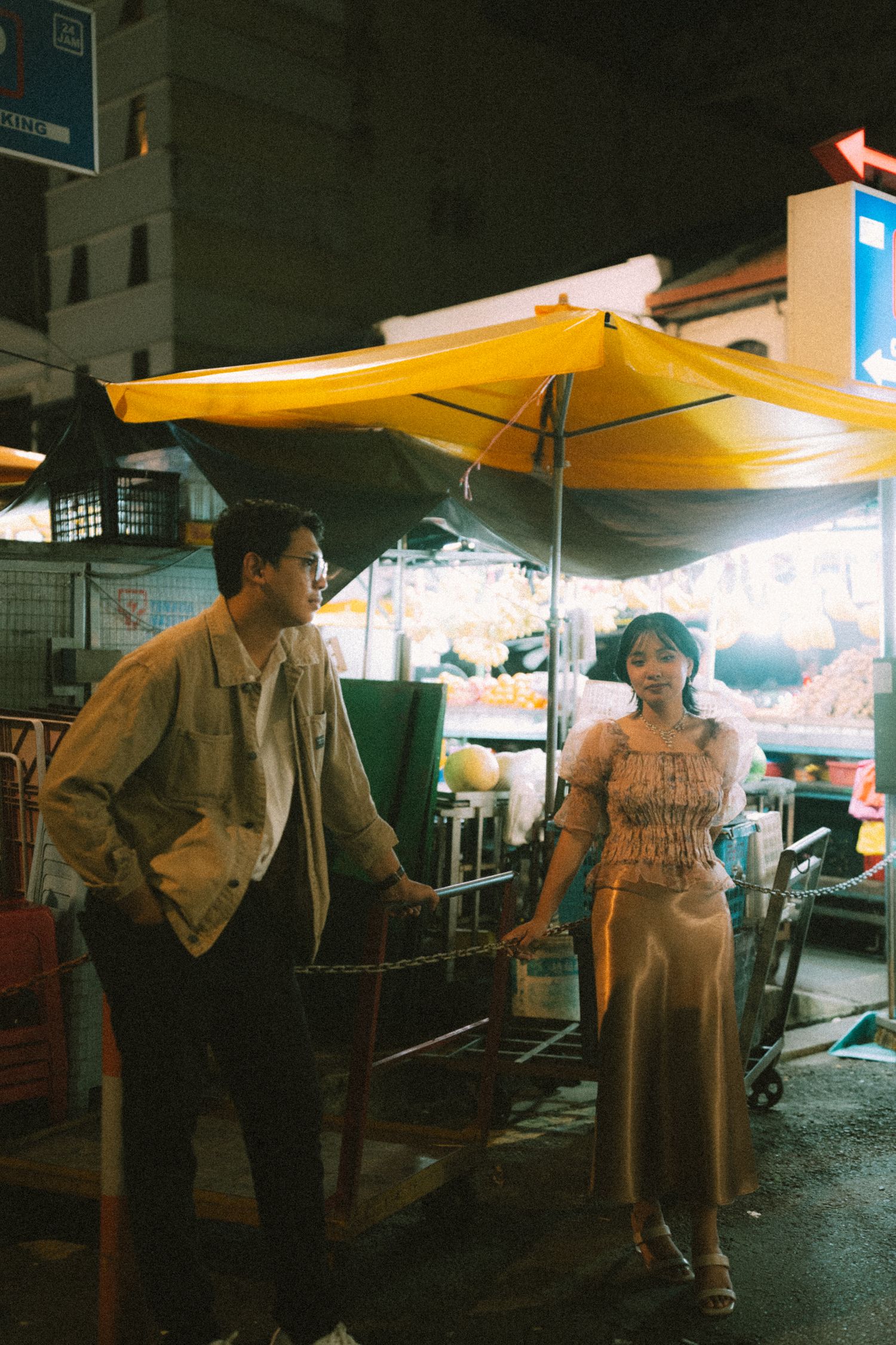 Couple standing under yellow awning at night market with street vendors visible.