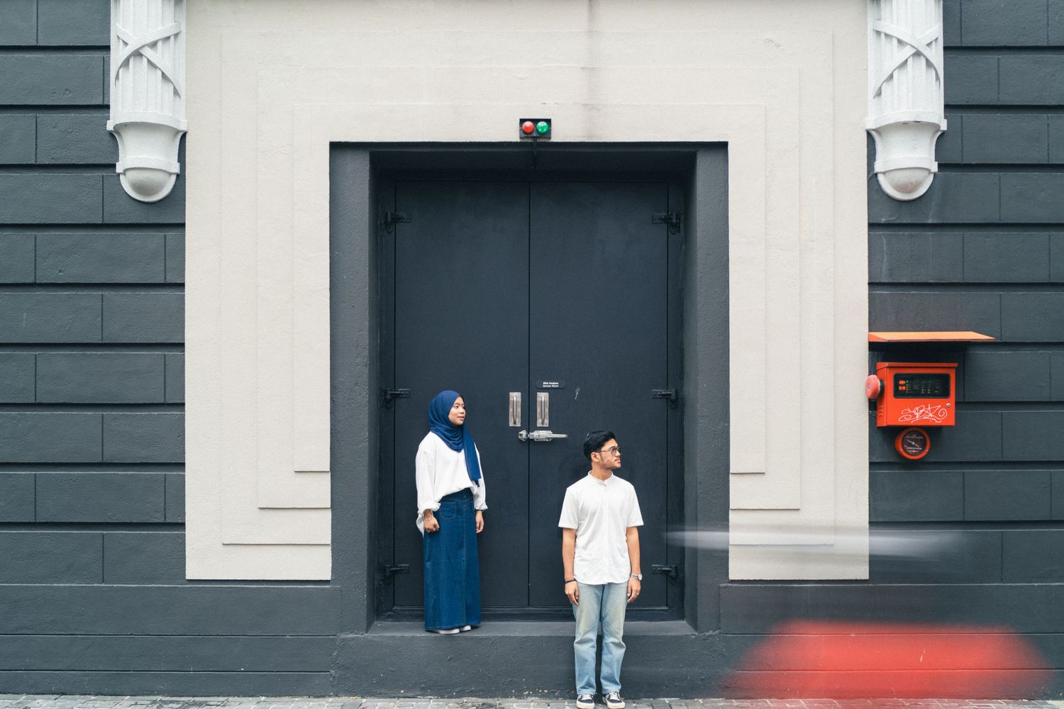 Two people stand in front of a modern black and white building entrance with security cameras.