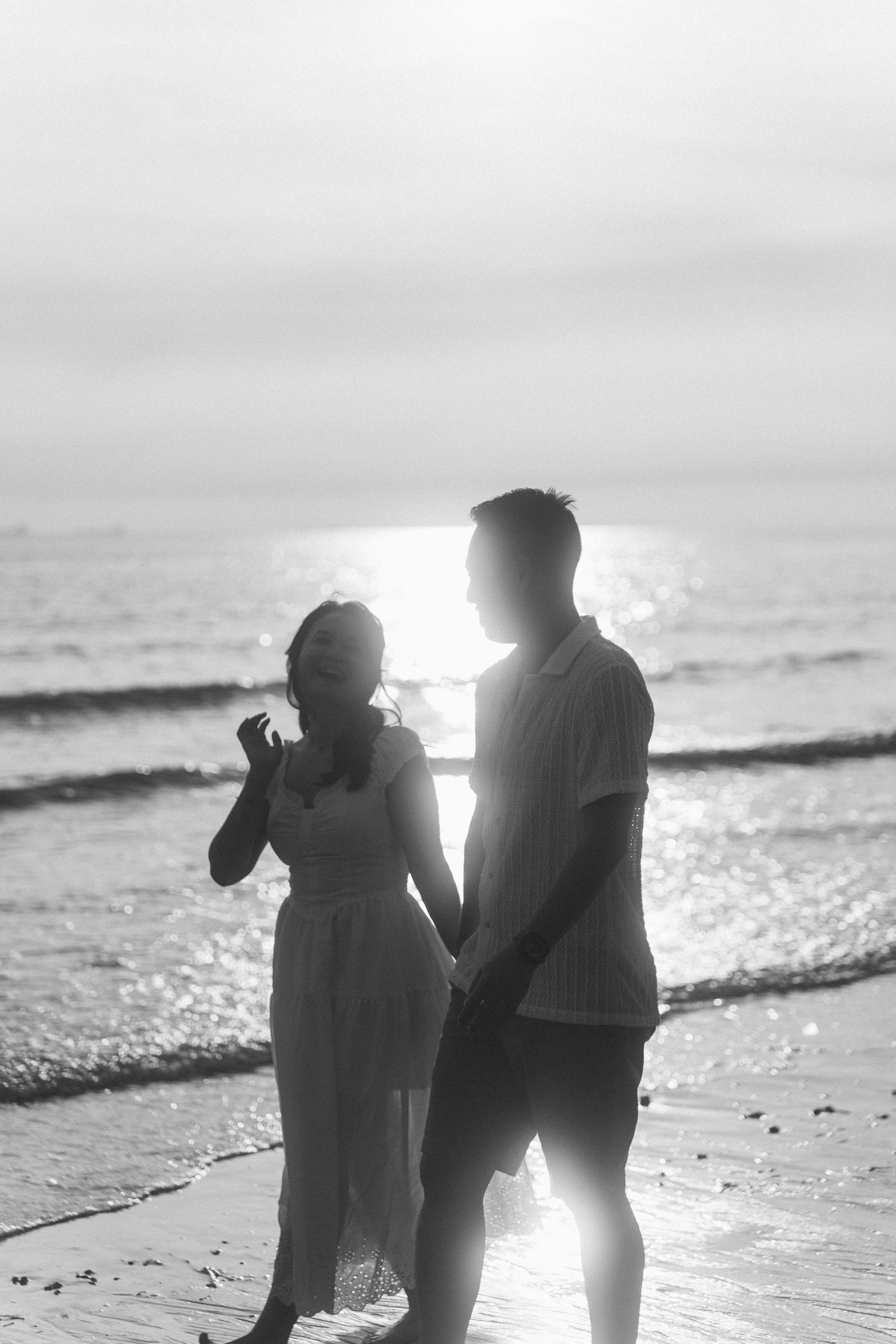 A silhouetted couple standing on beach at sunset with waves rolling in.