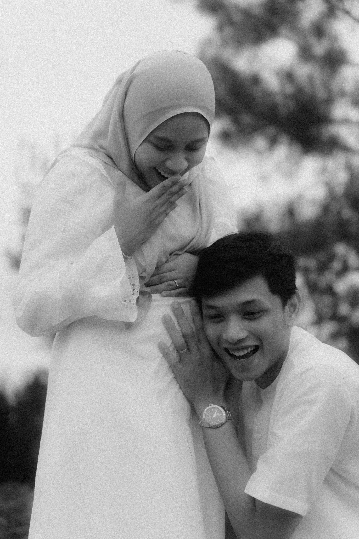 A candid black and white photo showing a joyful moment between a couple in white attire outdoors.