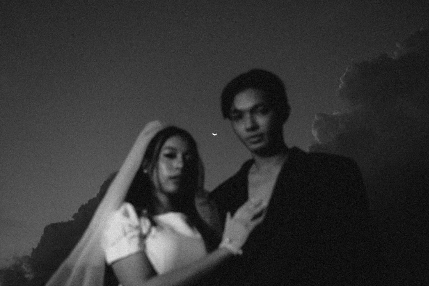 Moody black and white portrait of couple against evening sky.