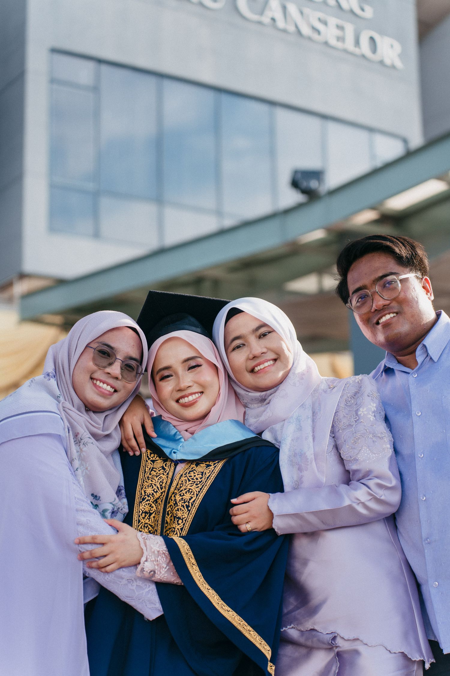 A group in traditional Malaysian attire celebrates a graduation ceremony outside a modern building.