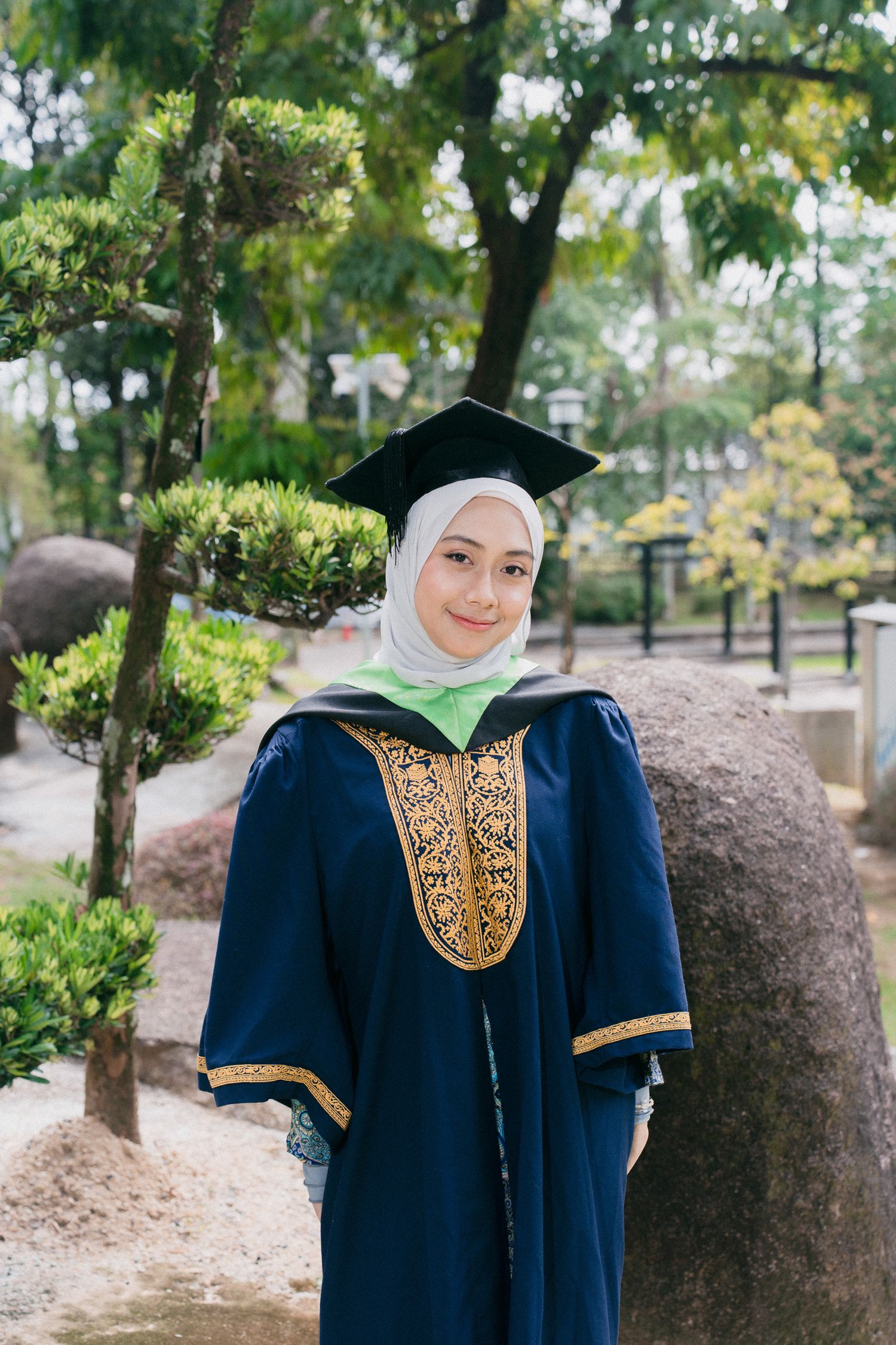 A navy blue graduation gown with gold embellishments shown in multiple angles outdoors against a natural backdrop.