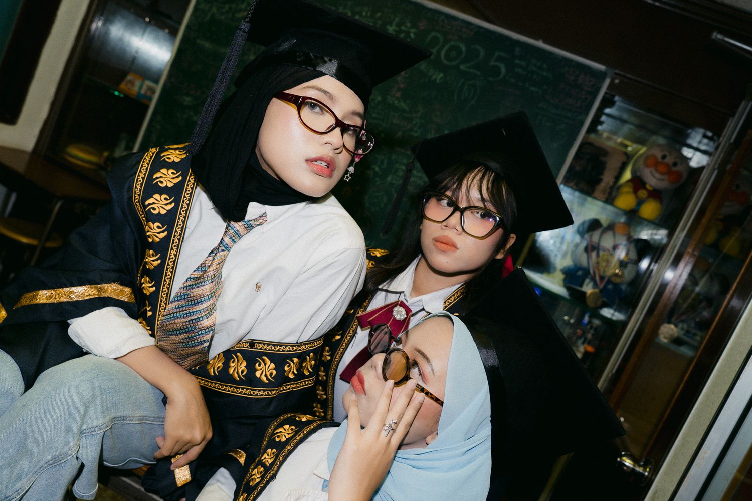 Two young women in graduation caps and gowns with glasses pose together at a graduation celebration.
