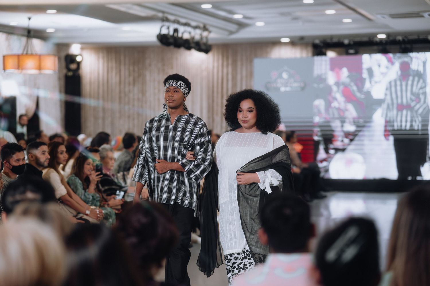 Models wearing avant-garde streetwear designs perform on runway with projected backdrop.