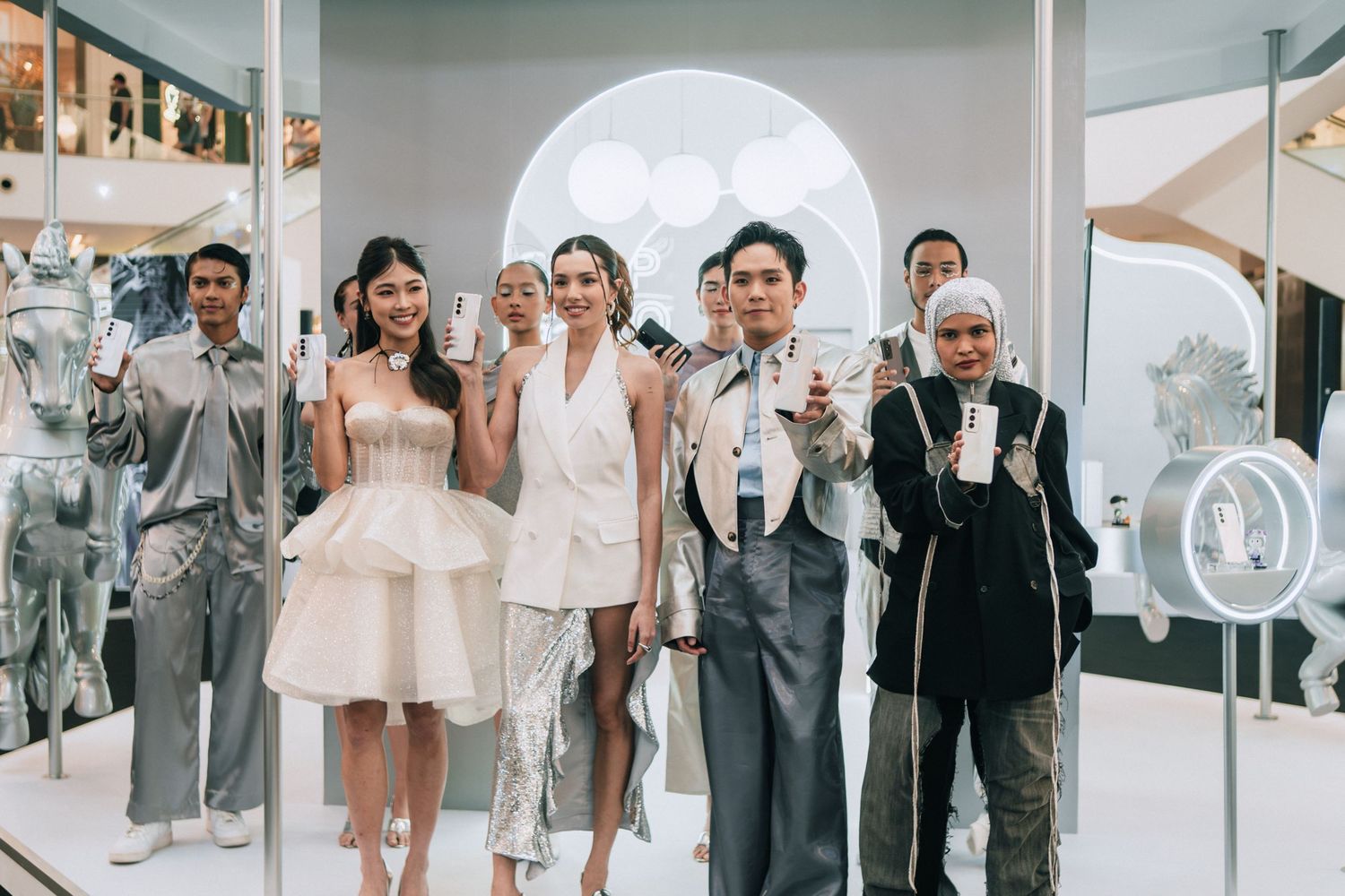 Group of models presenting fashion looks under a white arched backdrop with circular lighting.