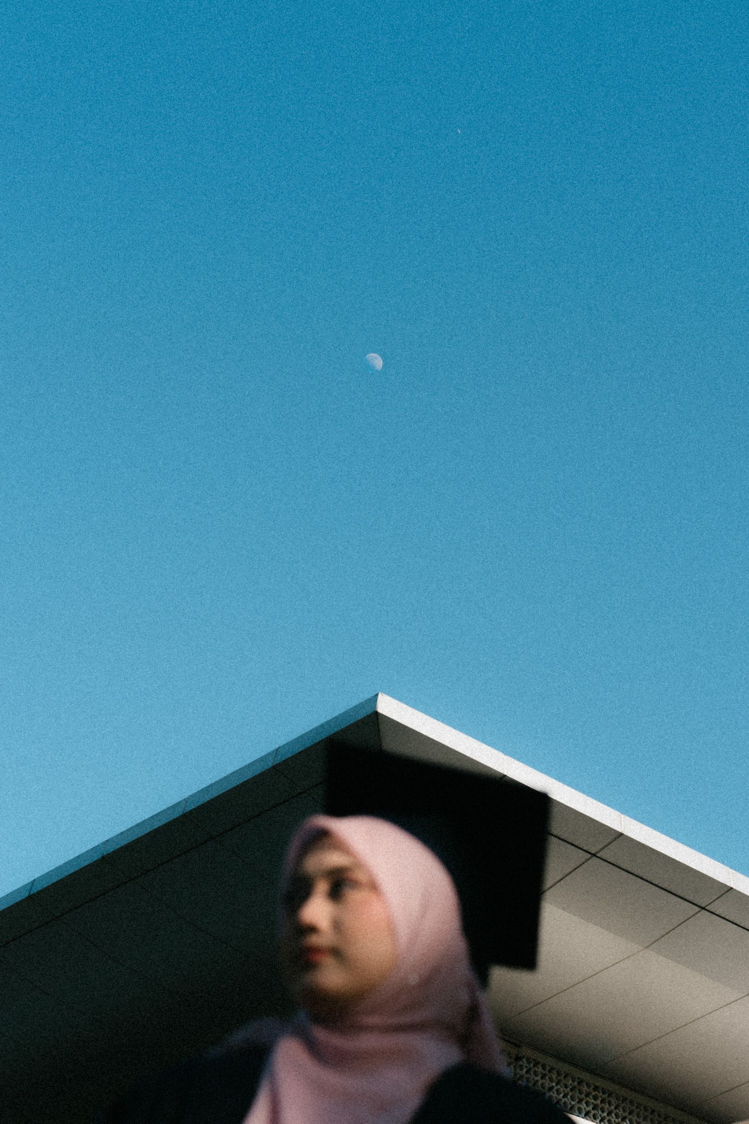 Minimalist architectural detail against bright blue sky with partial moon visible.