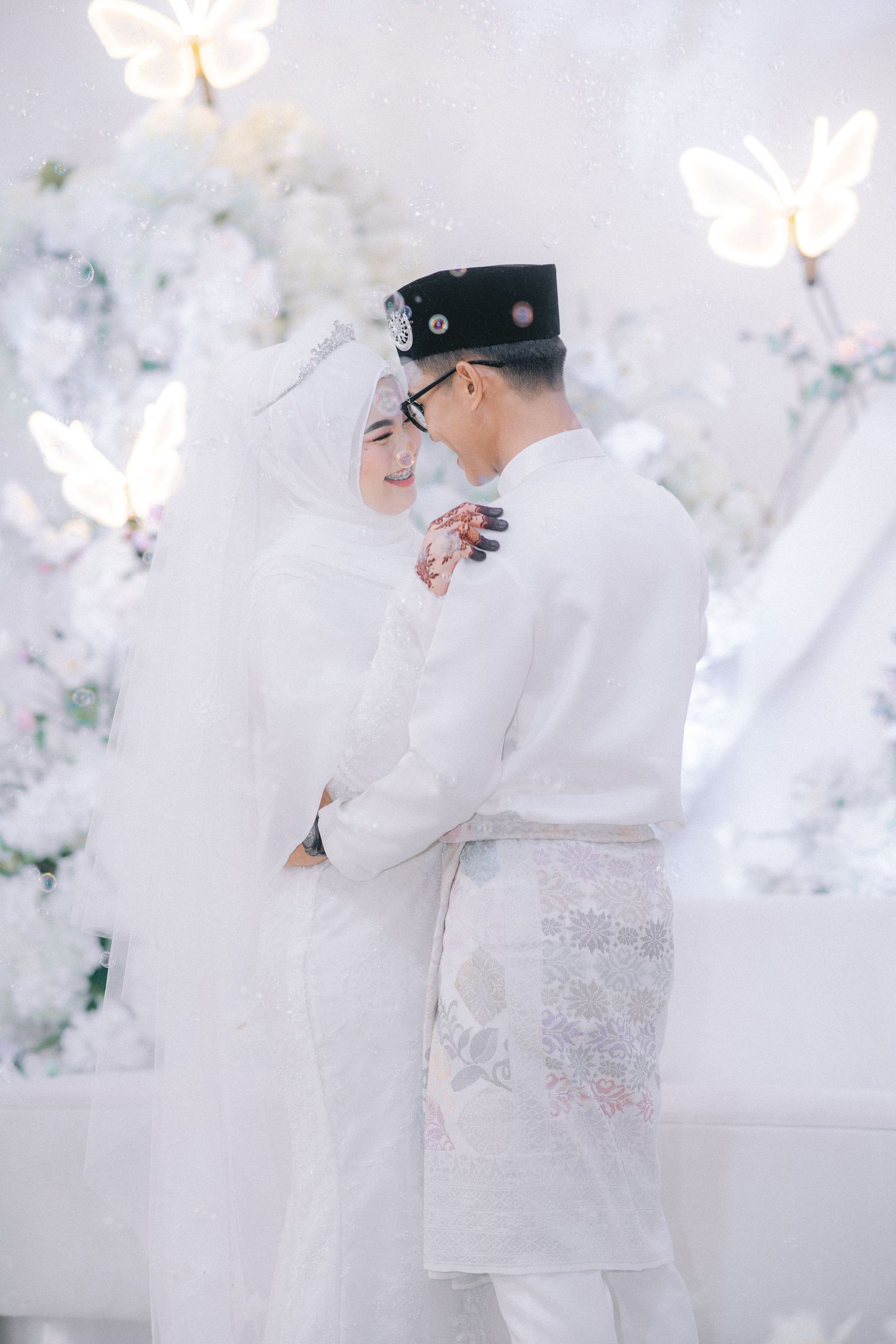 A couple in traditional white hanbok attire share romantic moments against a dreamy floral backdrop during their Korean wedding.