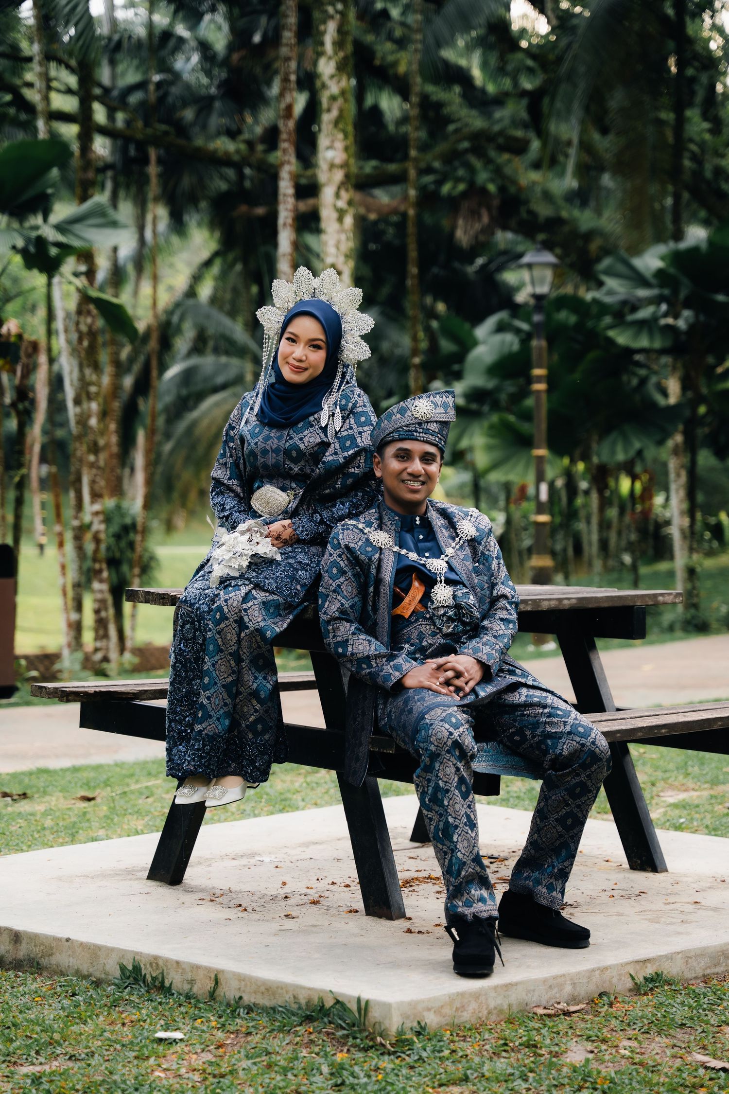A couple in matching navy patterned outfits sitting together on a park bench in a peaceful garden setting.