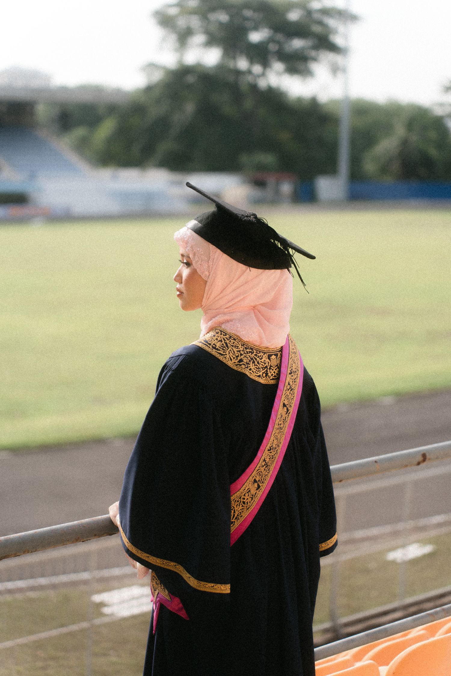A series of graduation portraits showing someone in black academic regalia with pink hijab against an outdoor field.