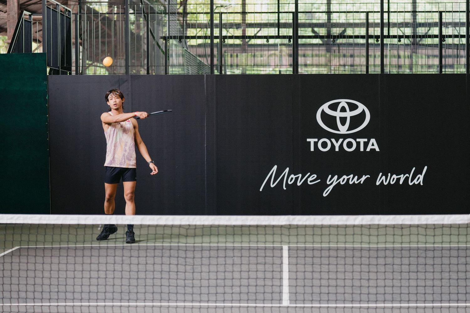 Tennis players practicing serves and volleys on an indoor court with Toyota branding visible on the walls.