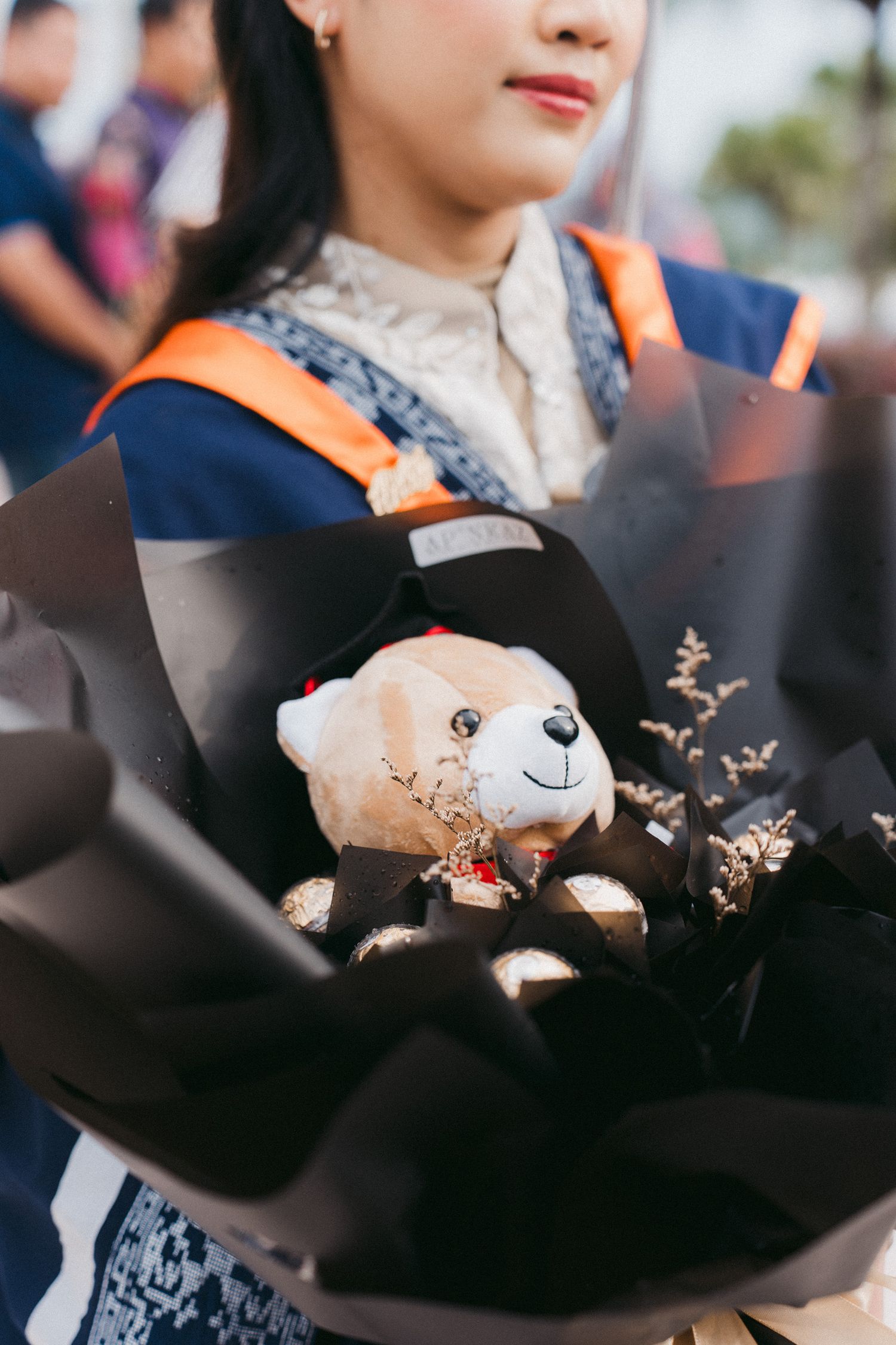 Close-up of graduation bouquet with plush teddy bear and dried flowers wrapped in black paper.