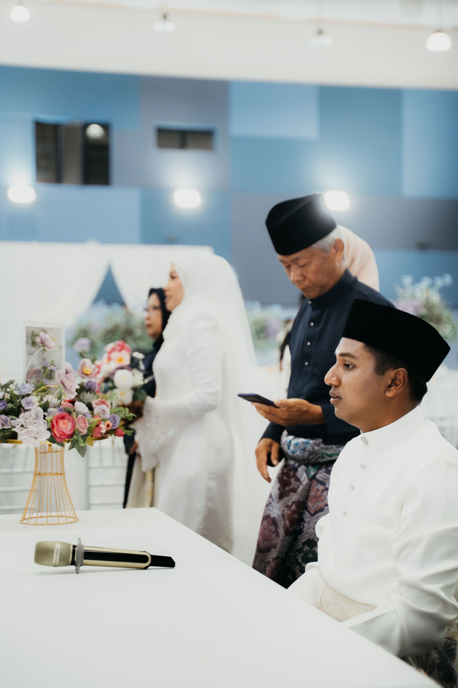 People in white traditional Muslim attire during a religious or cultural gathering with floral decorations.