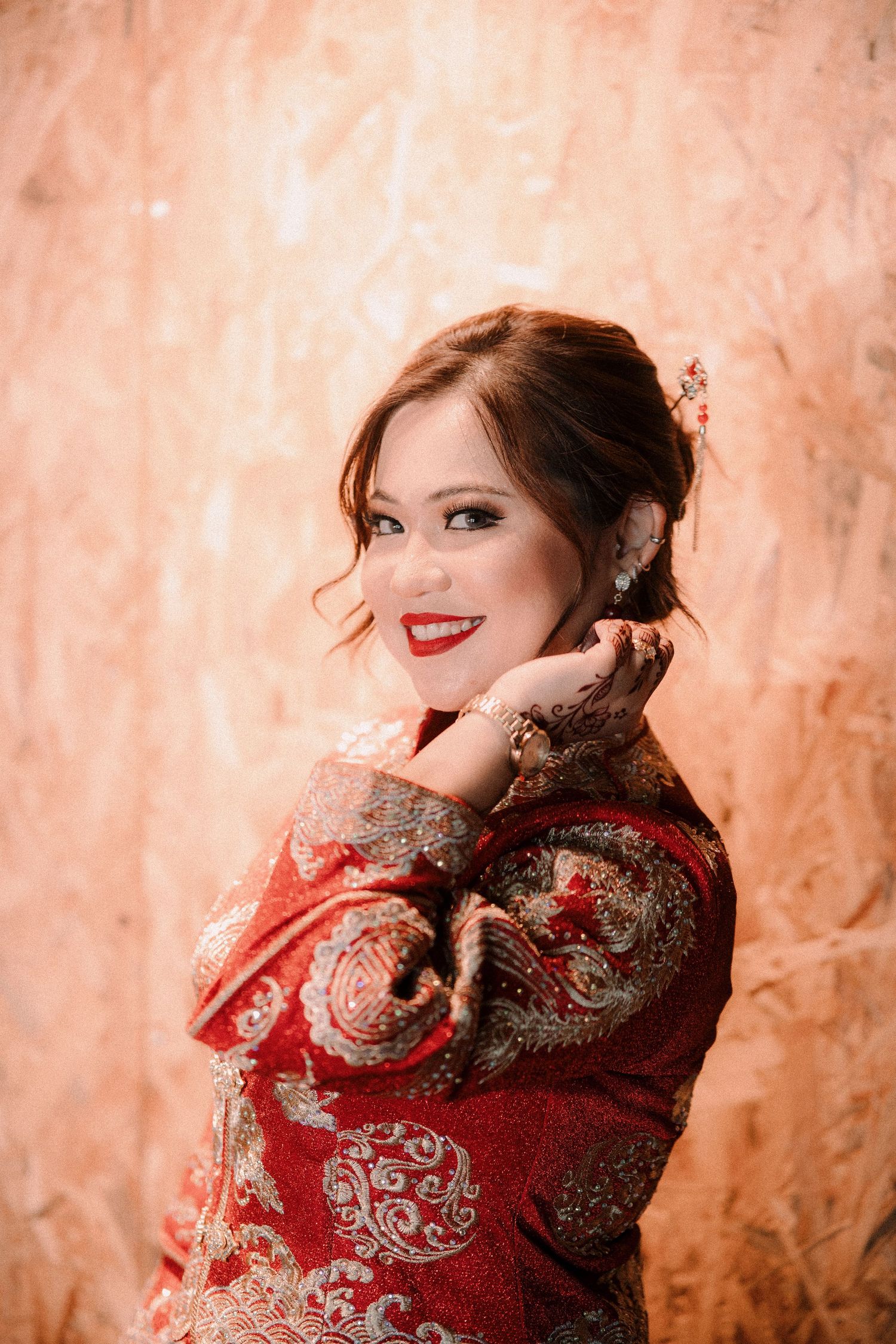 Portrait of a person wearing a red traditional Chinese qipao dress with intricate gold embroidery against textured wall.