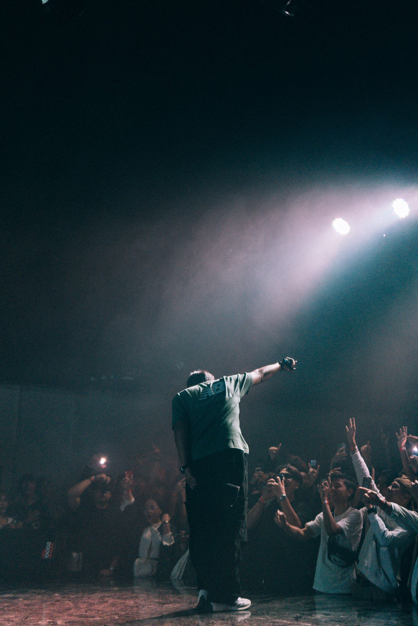 Concert performer silhouetted against bright spotlights with crowd reaching up from below.