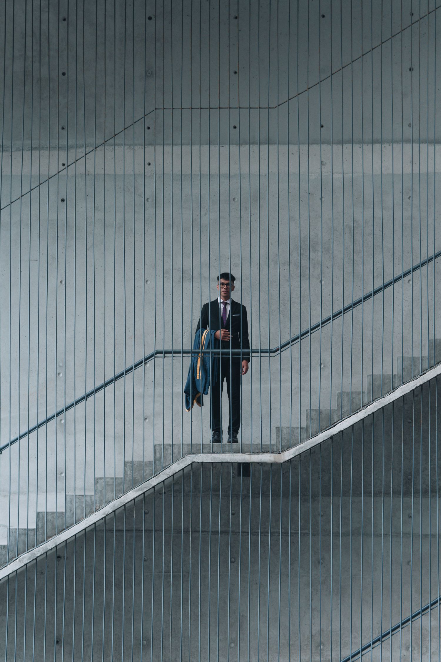 A lone figure stands on geometric stairs against an industrial striped wall background.