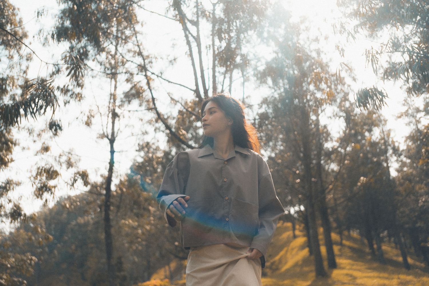 Person in casual clothing enjoying a sunlit moment in a eucalyptus forest.